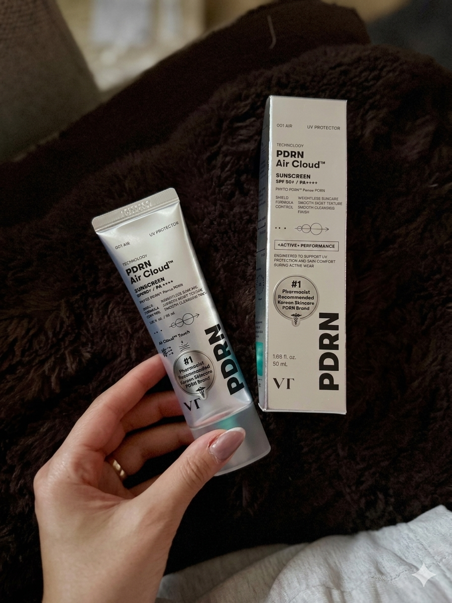Hand holding VT PDRN Air Cloud sunscreen and its box with a visible Pharmacist Recommended mark